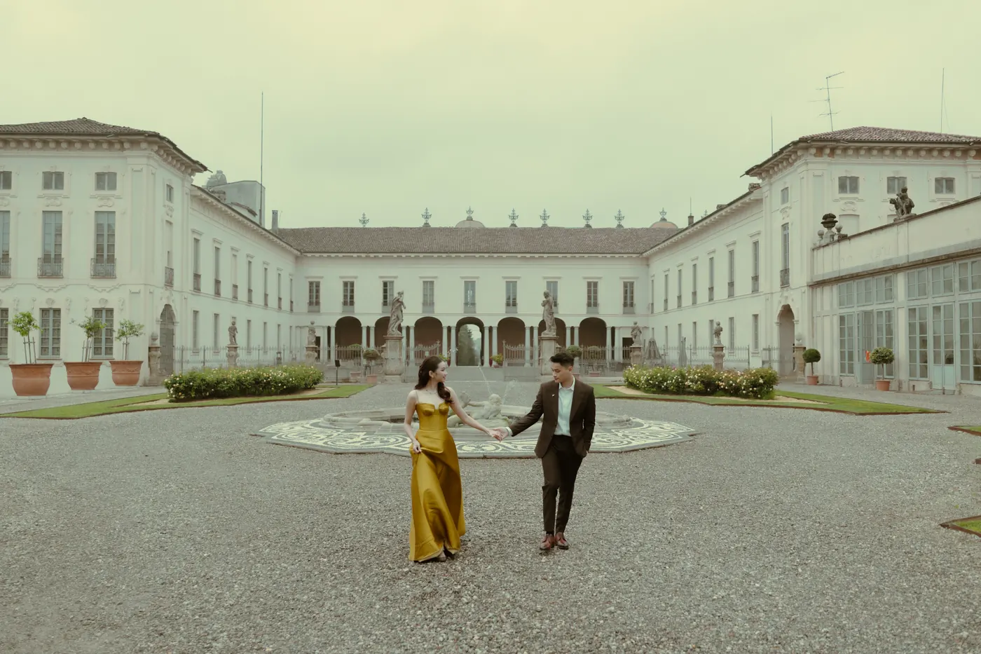 Karin in a golden gown and Matthew holding hands in a villa courtyard